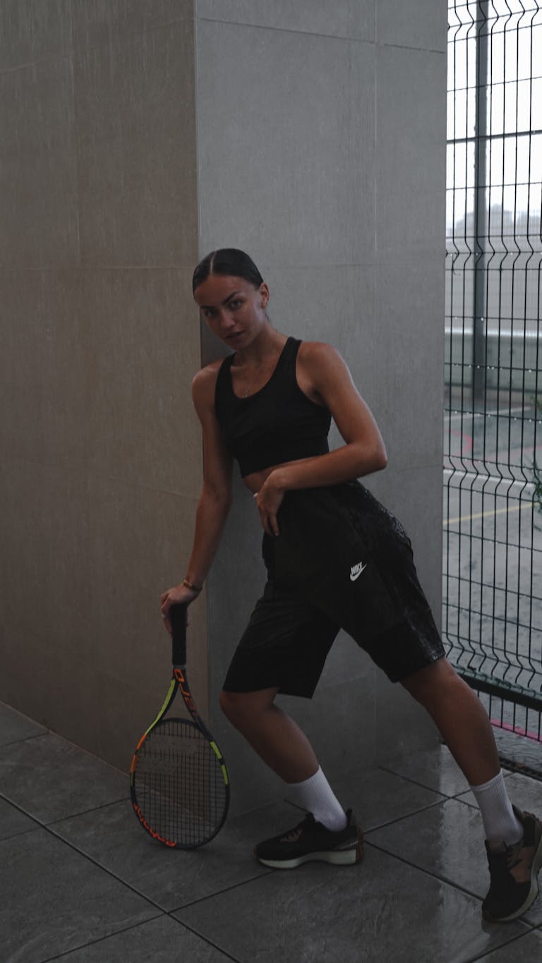Athletic woman posing with a tennis racket indoors, showcasing sportswear fashion.