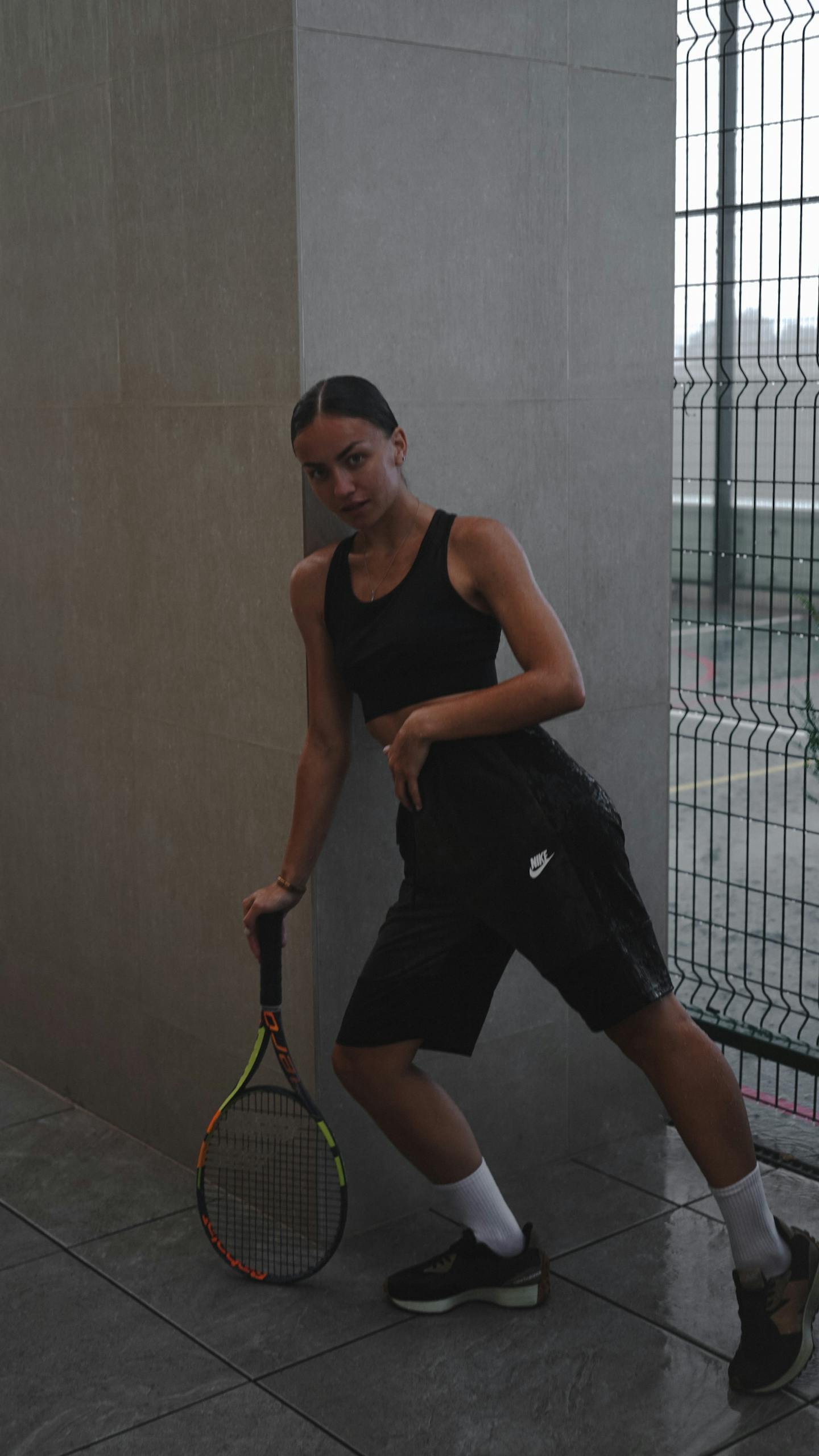 Athletic woman posing with a tennis racket indoors, showcasing sportswear fashion.