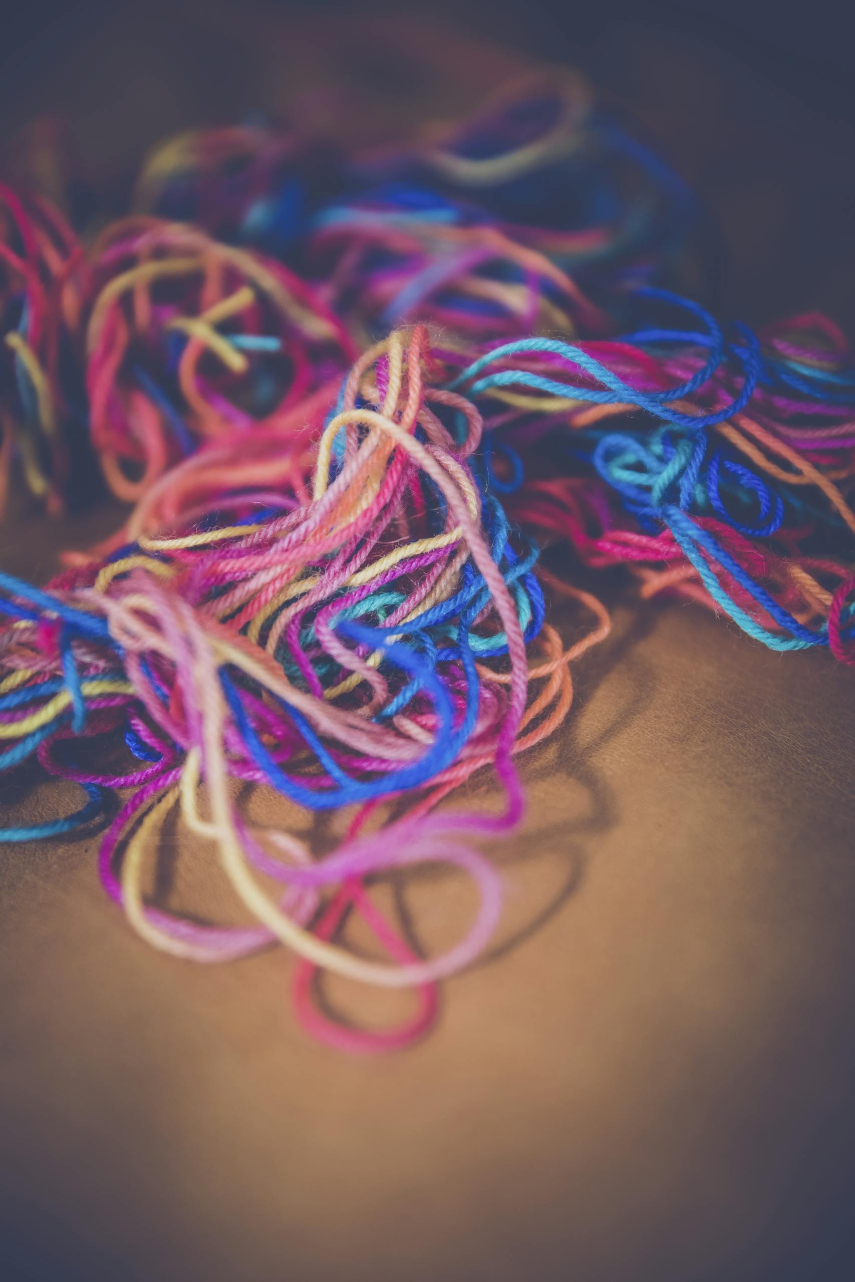 A close-up of colorful yarn strands in various hues on a brown backdrop, perfect for craft and DIY themes.