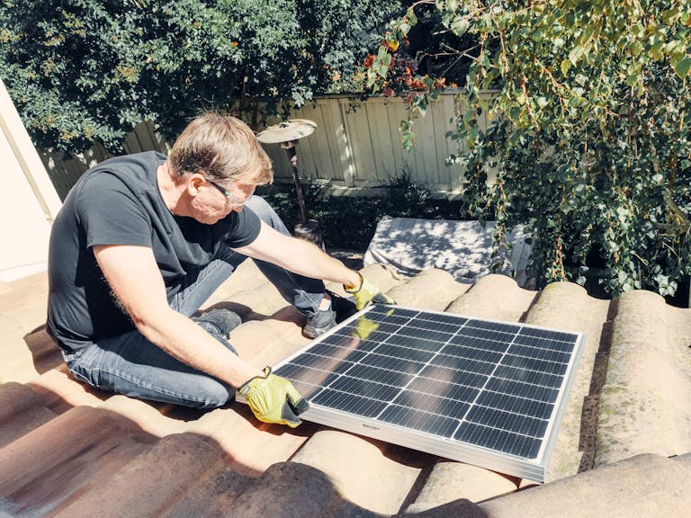 Male technician installing solar panel on roof, promoting sustainable energy.