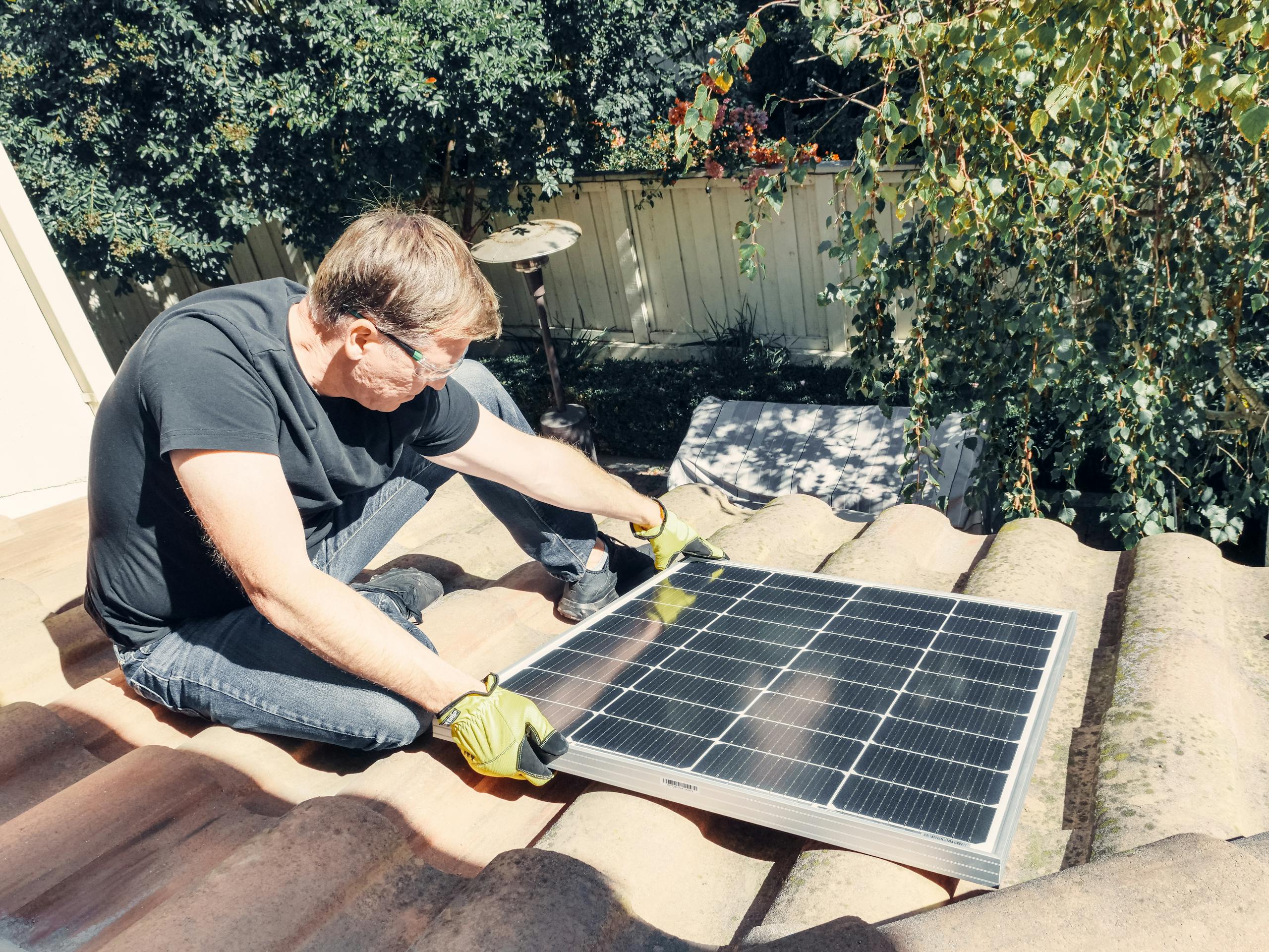 Male technician installing solar panel on roof, promoting sustainable energy.